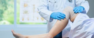 close-up-hand-wear-medical-gloves-doctor-examining-head-patient-with-knee-problems-clinic-min