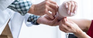 closeup-man-doctor-with-wrapping-nurse-bandages-splint-arm-female-patient-wear-arm-splint-with-analogue-pressure-gauge-better-healing-room-hospital-background-min